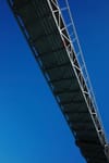 A bridge with a metal framework against a clear blue sky, viewed from below