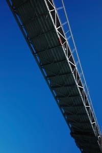 A bridge with a metal framework against a clear blue sky, viewed from below
