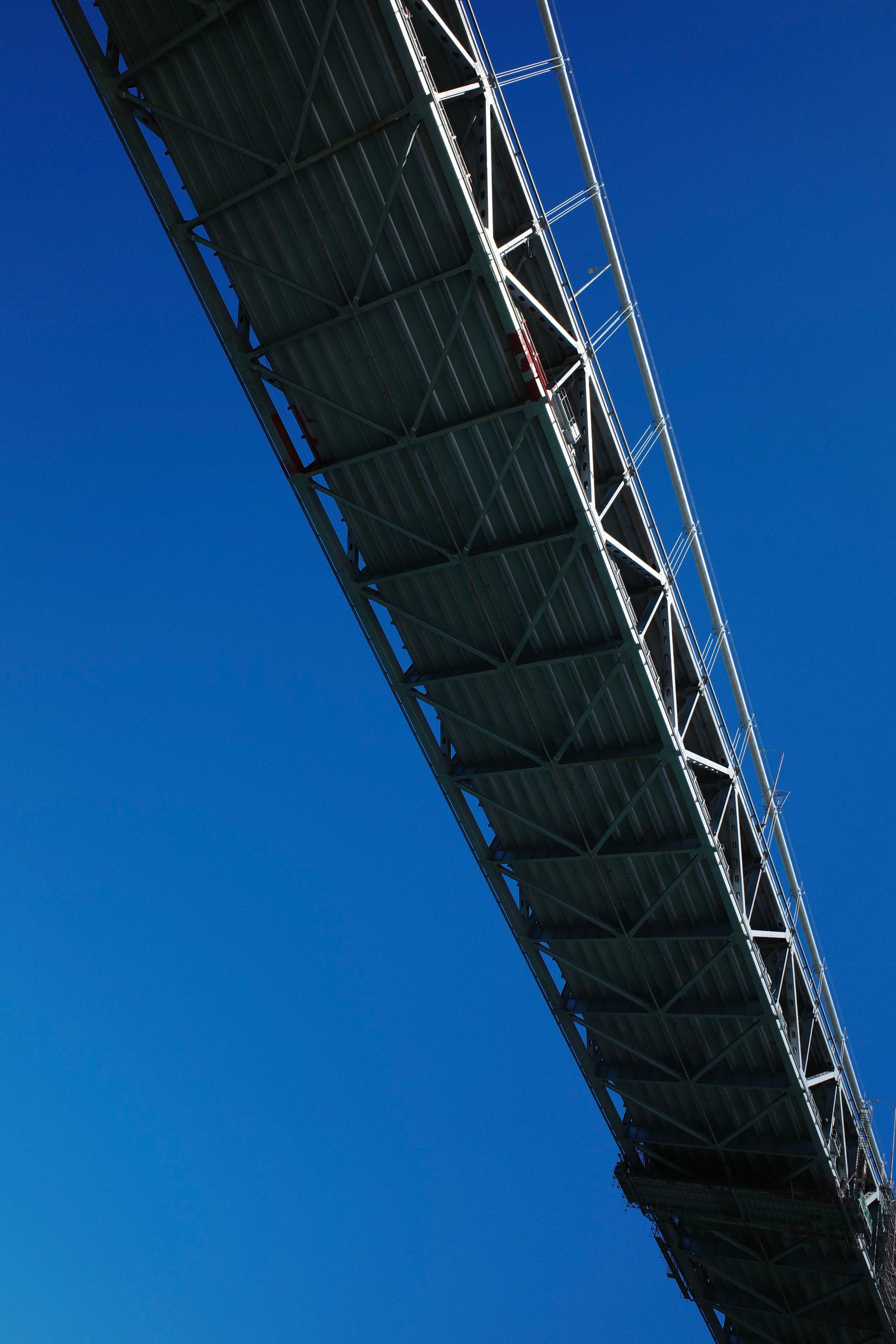 A bridge with a metal framework against a clear blue sky, viewed from below