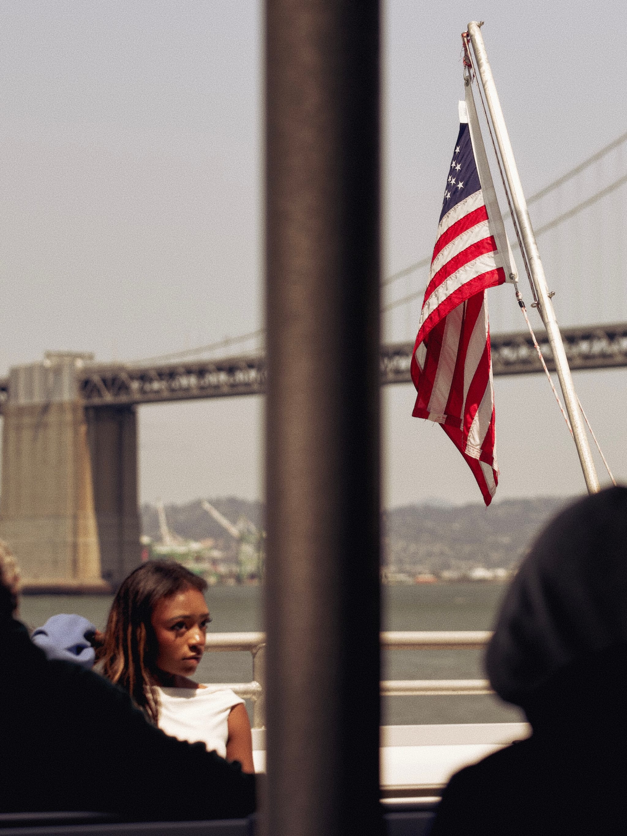 A woman on a boat with an American flag, a bridge, and water in the background