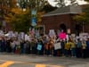 A large crowd lines a sidewalk in front of a brick building, holding protest signs and American flags on an autumn day