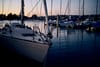 A marina at dusk with sailboats docked, reflecting on calm water