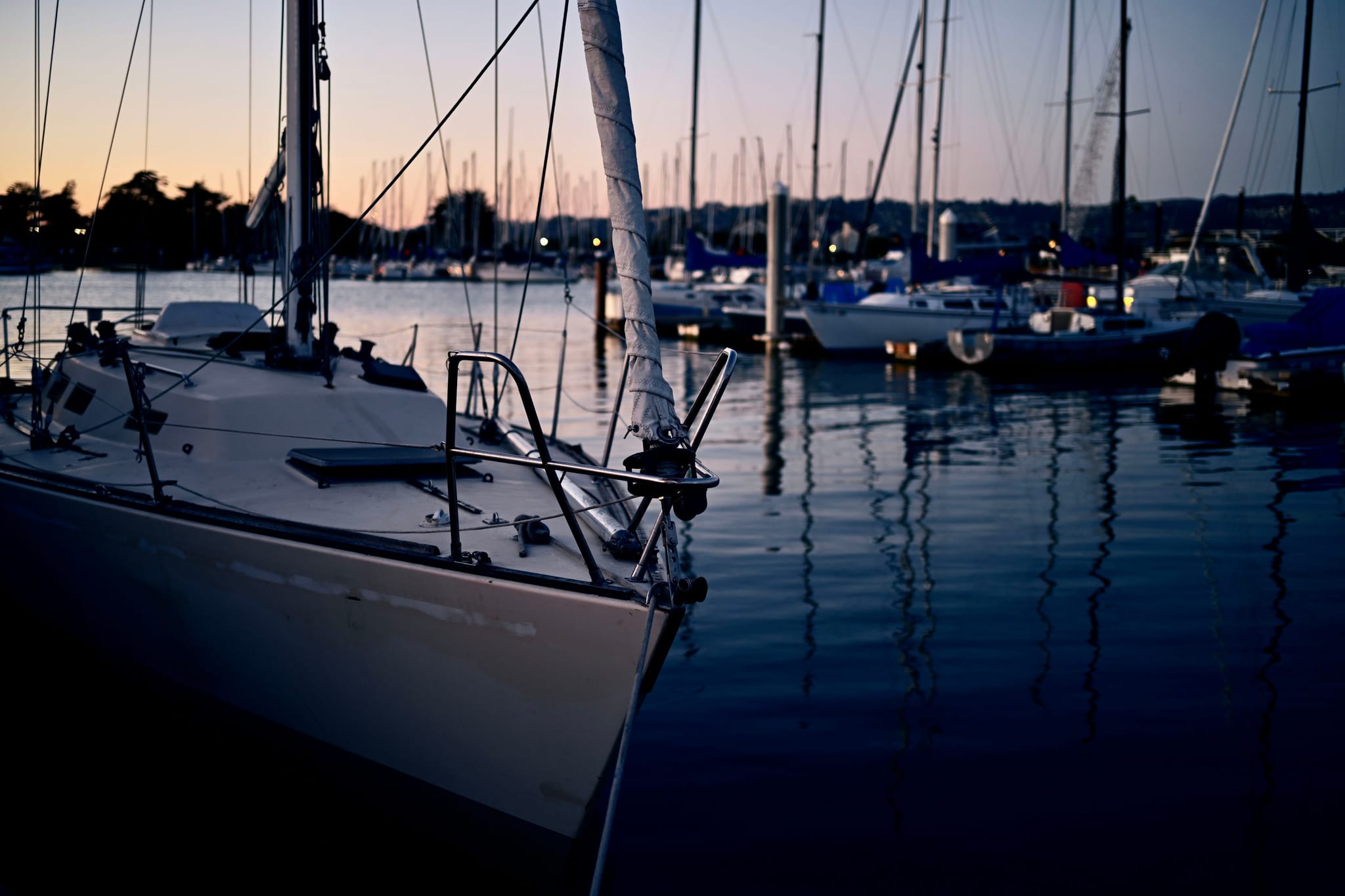 A marina at dusk with sailboats docked, reflecting on calm water