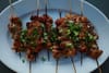 Grilled skewers of meat garnished with chopped green onions on a white plate