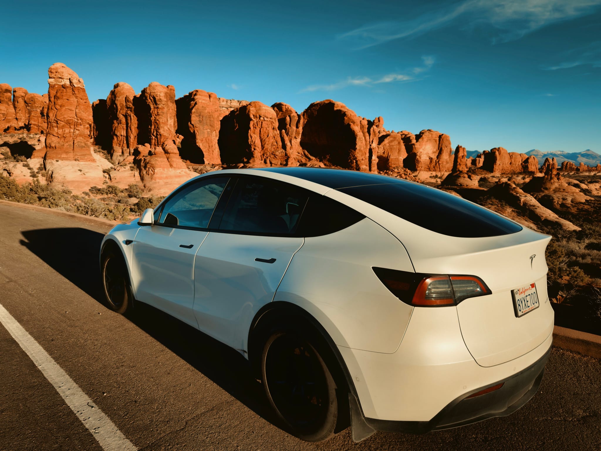 White Tesla parked on a desert road beside red rock formations