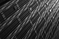 A black and white abstract view of a building facade with a pattern of windows and panels, captured at an angle