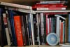 A bookshelf filled with various photography books, some stacked horizontally and others vertically, with a small decorative plate in front