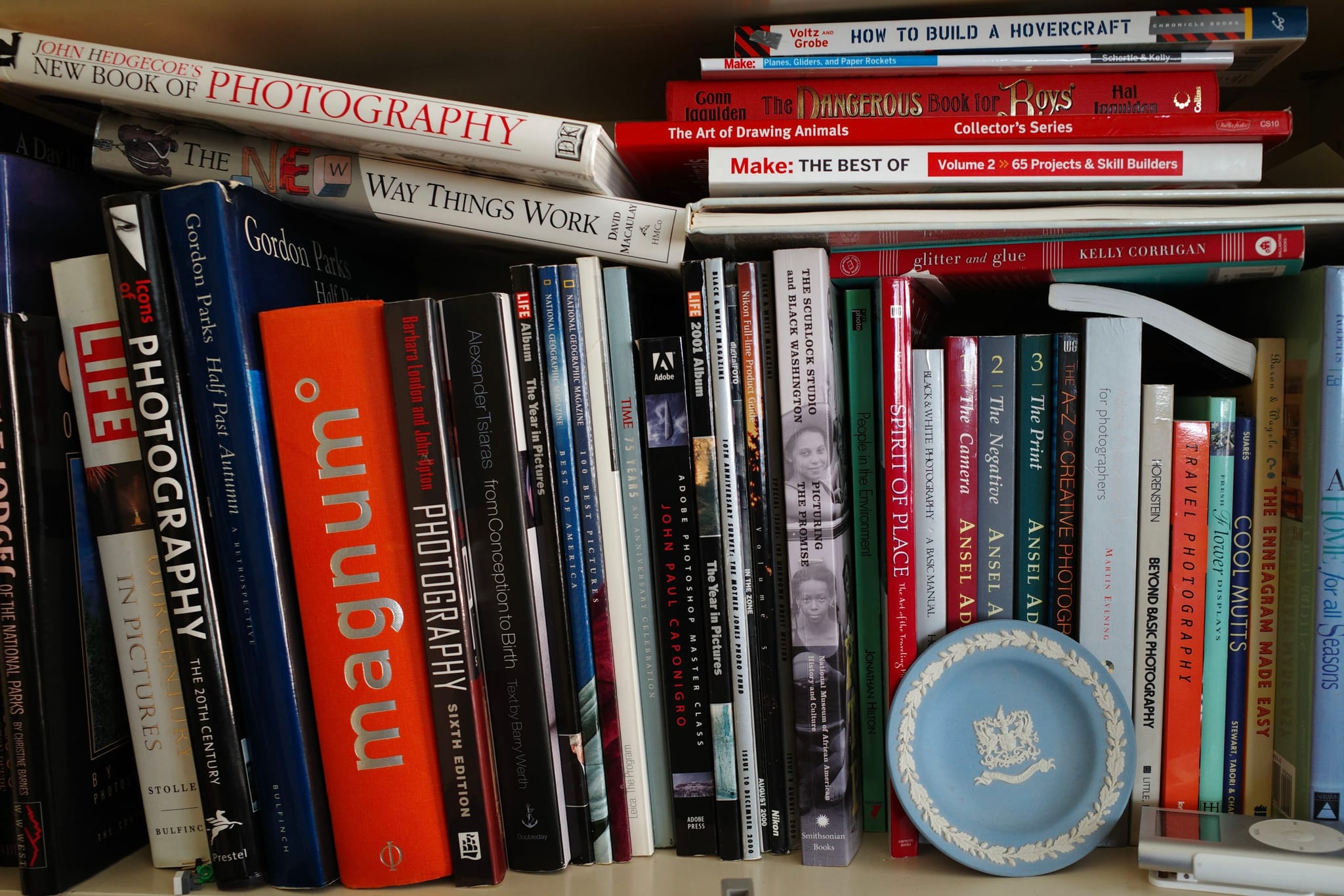 A bookshelf filled with various photography books, some stacked horizontally and others vertically, with a small decorative plate in front