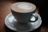 A cup of coffee with latte art on a white saucer, placed on a wooden surface
