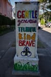 A painted utility box with the words GENTLE, generous, TRUTHFUL, kind, BRAVE in colorful letters, featuring a fleur-de-lis symbol and grass at the bottom