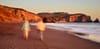 Two people walking along a beach at sunset with cliffs in the background