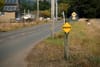 A rural road with a yellow diamond-shaped sign that reads BREATHE, surrounded by grass and trees, with houses in the background
