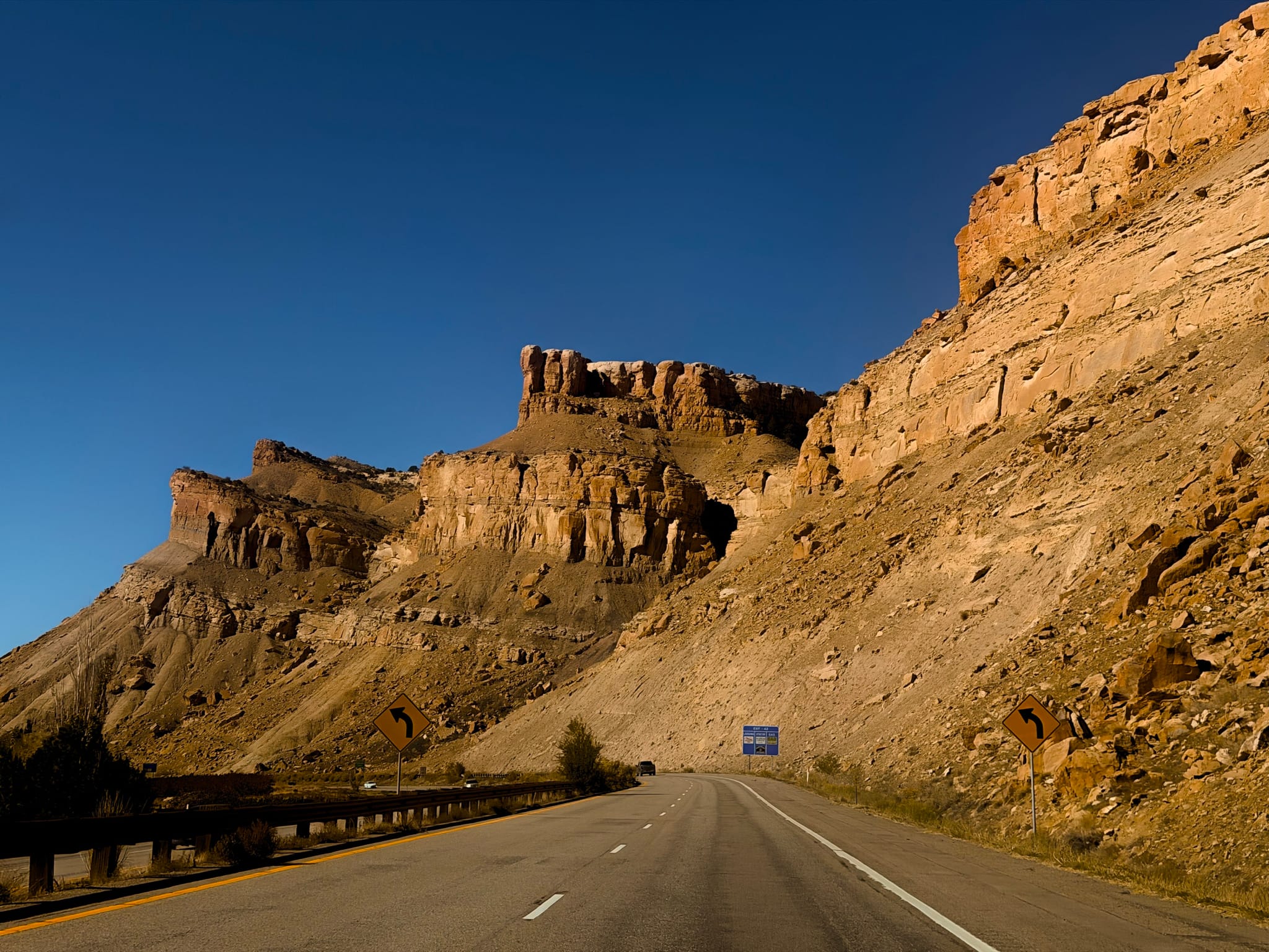 Open highway beneath steep cliffs under a clear blue sky