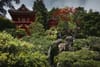A traditional Japanese garden with lush greenery, a small waterfall, and a red pagoda-style building in the background
