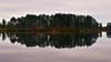 Still lake reflecting a tree-lined shoreline with autumn colors beneath an overcast sky