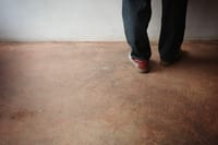 A person wearing jeans and sneakers walking on a textured floor near a plain wall