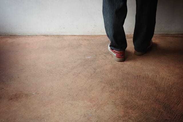 A person wearing jeans and sneakers walking on a textured floor near a plain wall