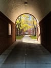 Brick archway framing a sunlit courtyard with trees and red-brick buildings