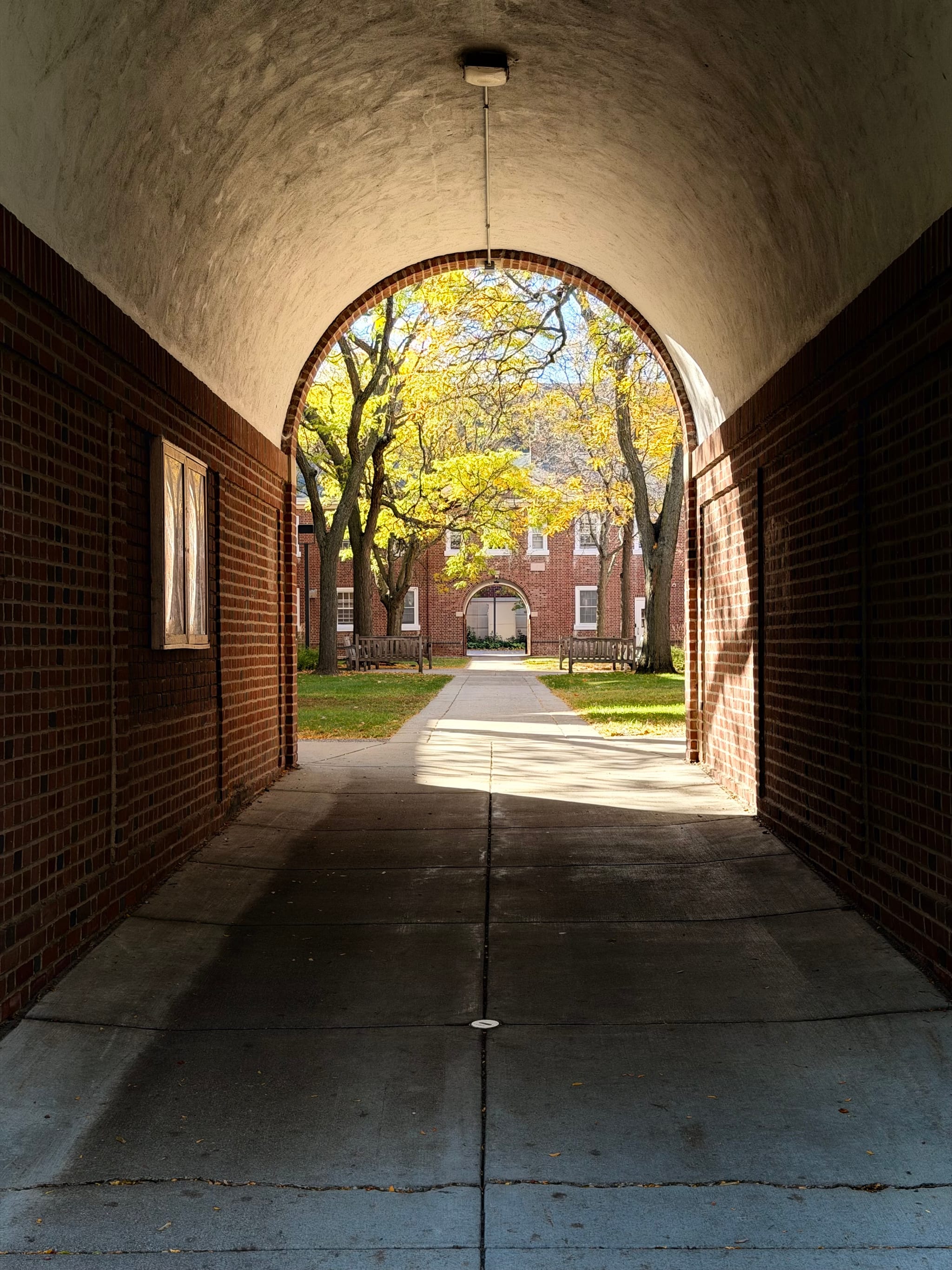 Brick archway framing a sunlit courtyard with trees and red-brick buildings