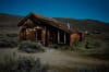 An old, weathered wooden cabin stands in a desolate, grassy landscape under a clear blue sky