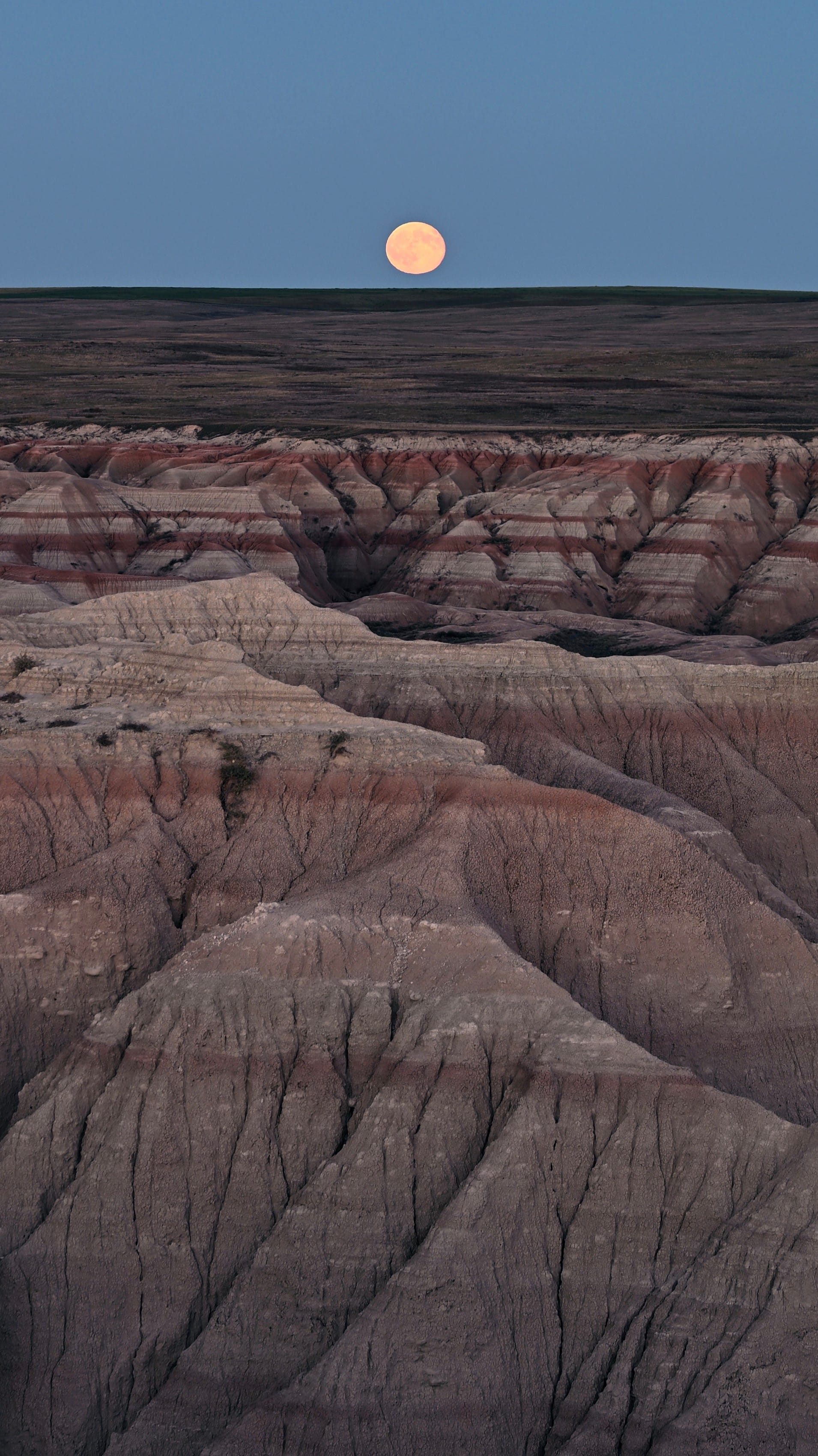 Full moon above a rugged, layered badlands landscape at dusk