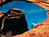 Bride and groom beneath a sandstone arch, veil flowing against deep blue sky