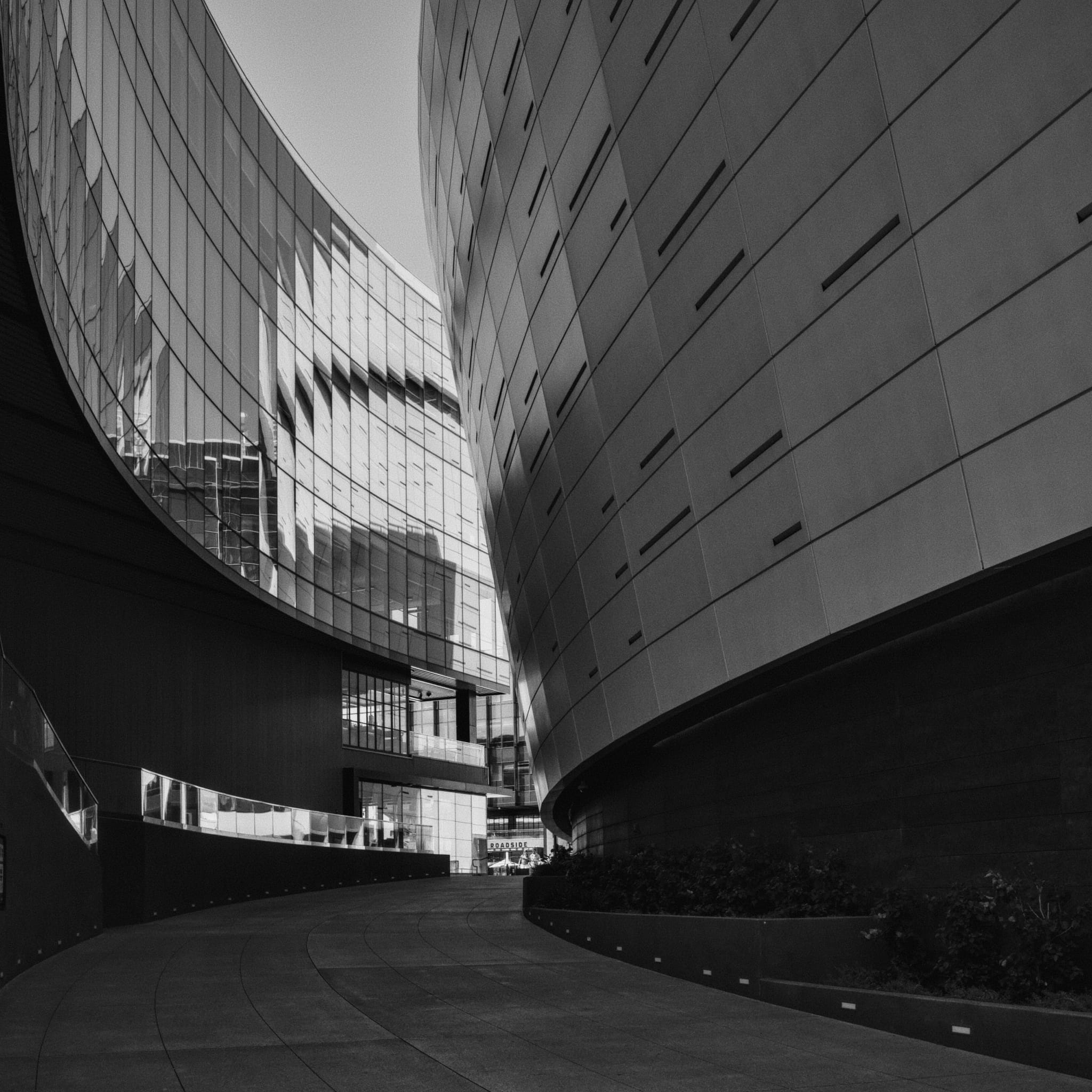 A black and white photograph of a modern architectural scene with curved buildings and a pathway between them