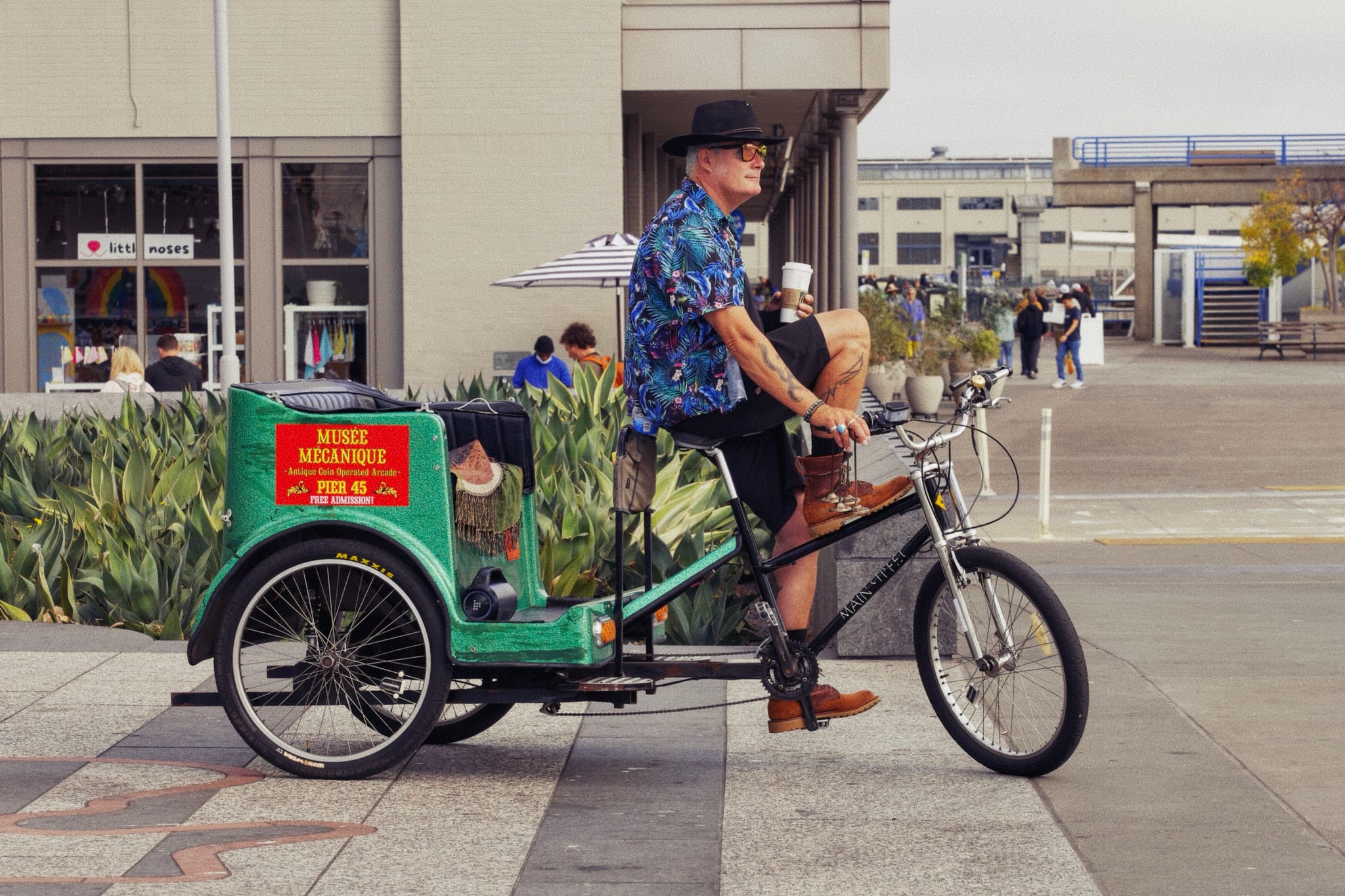 A man wearing a hat and a blue shirt rides a green pedicab on a city street