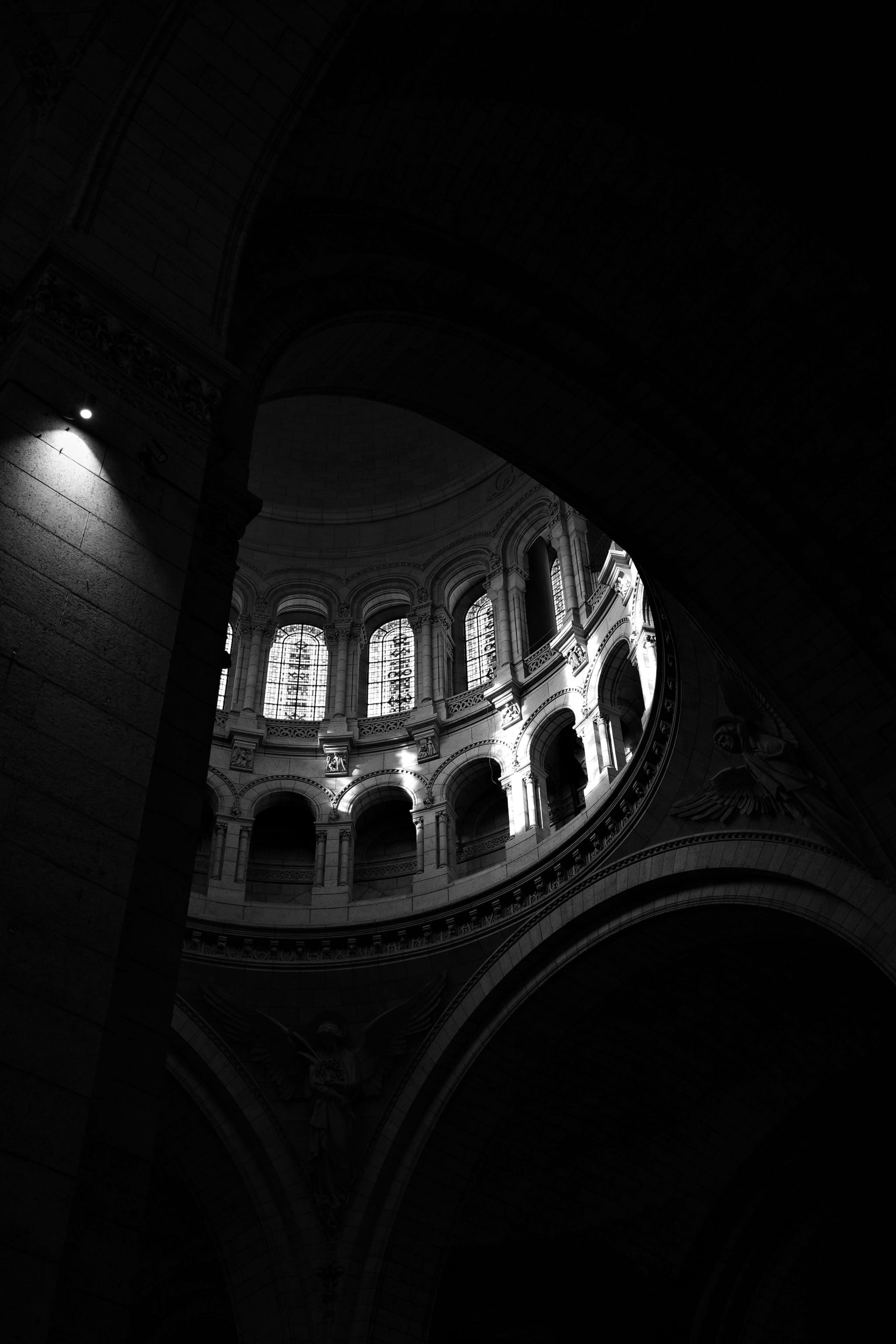 A dimly lit interior of a domed structure with arched windows, casting light and shadows