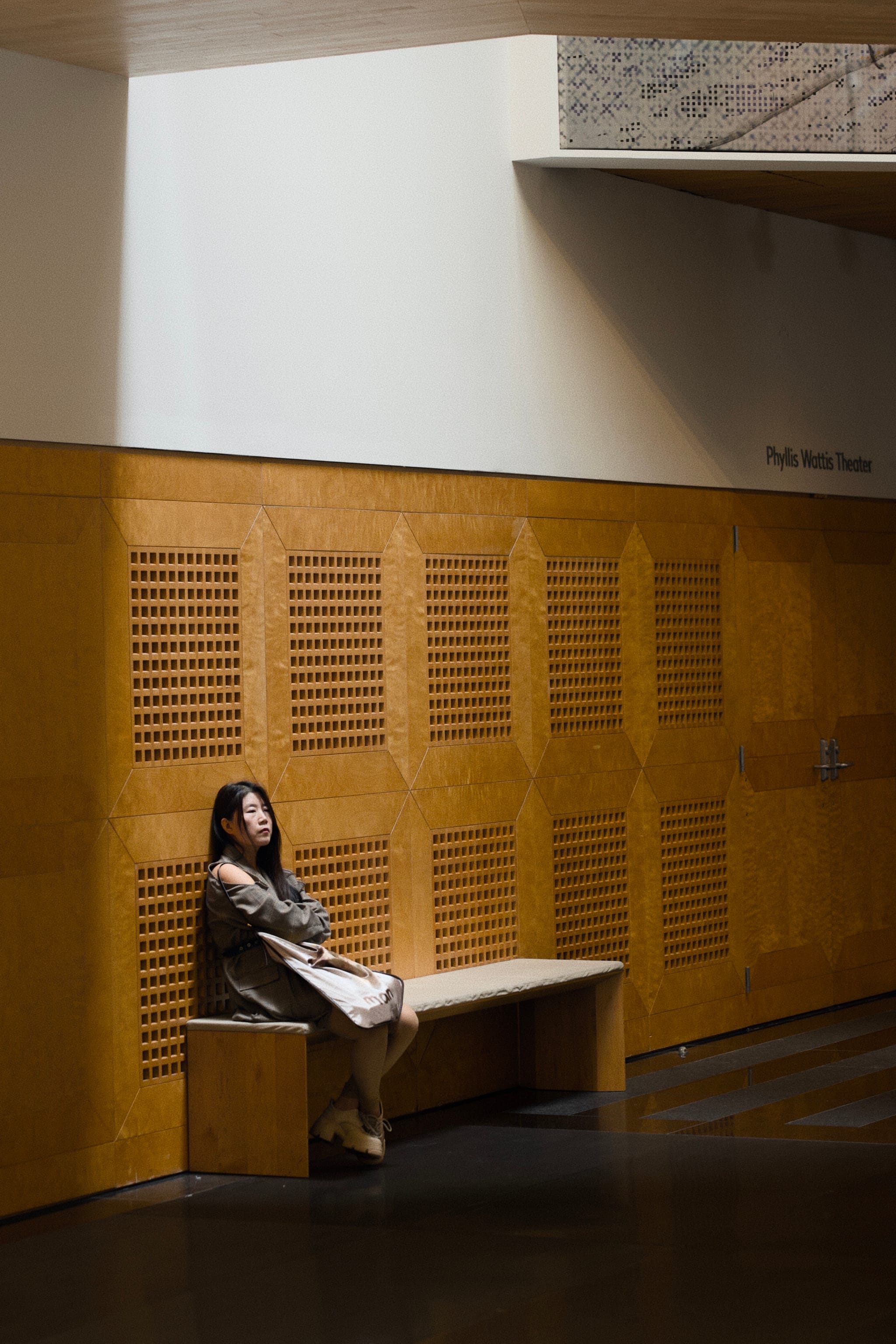 A person sitting on a bench in a dimly lit room with wooden paneling and a beam of light illuminating them