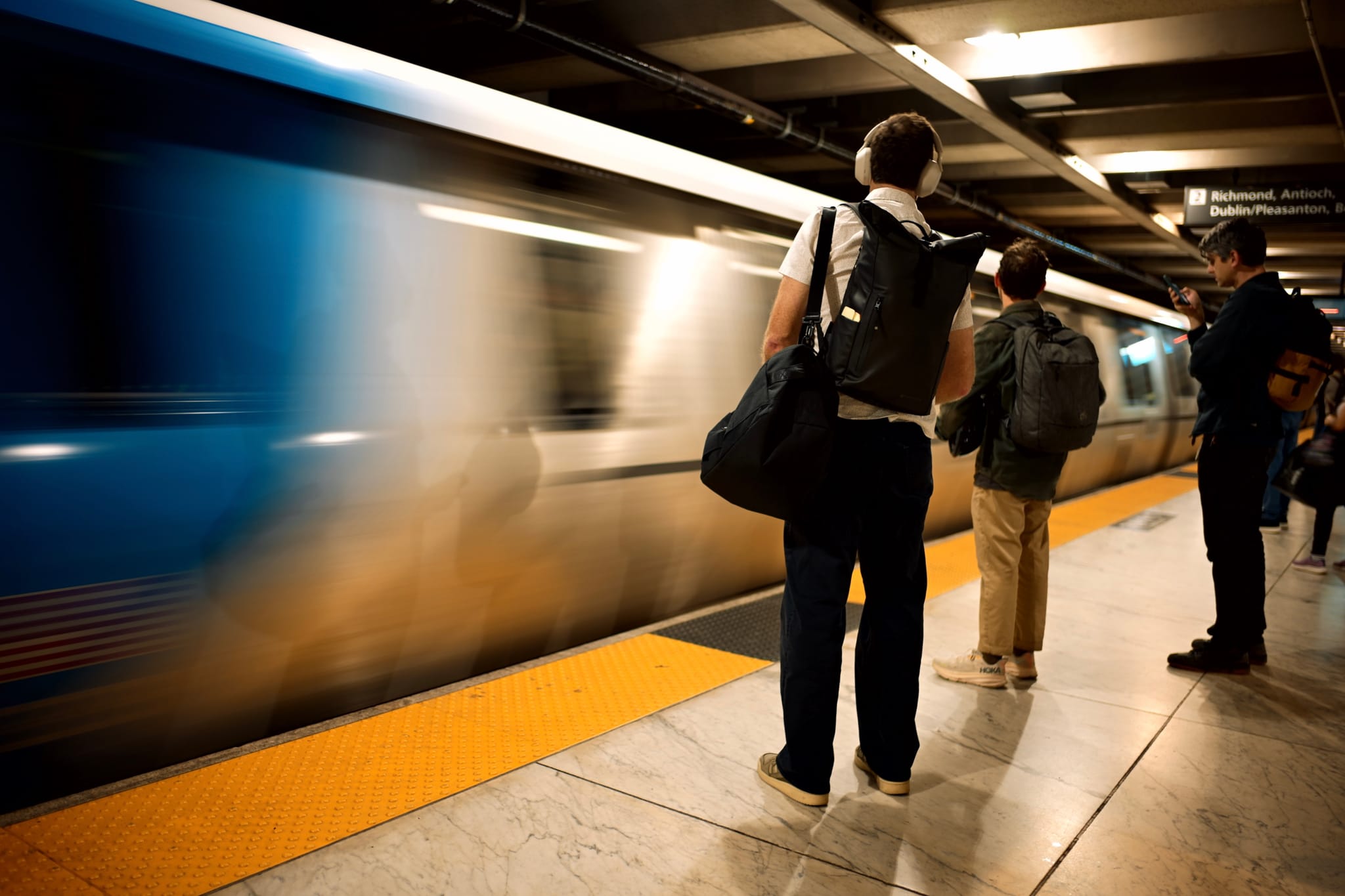 A subway platform with people waiting as a train speeds by, creating a motion blur effect