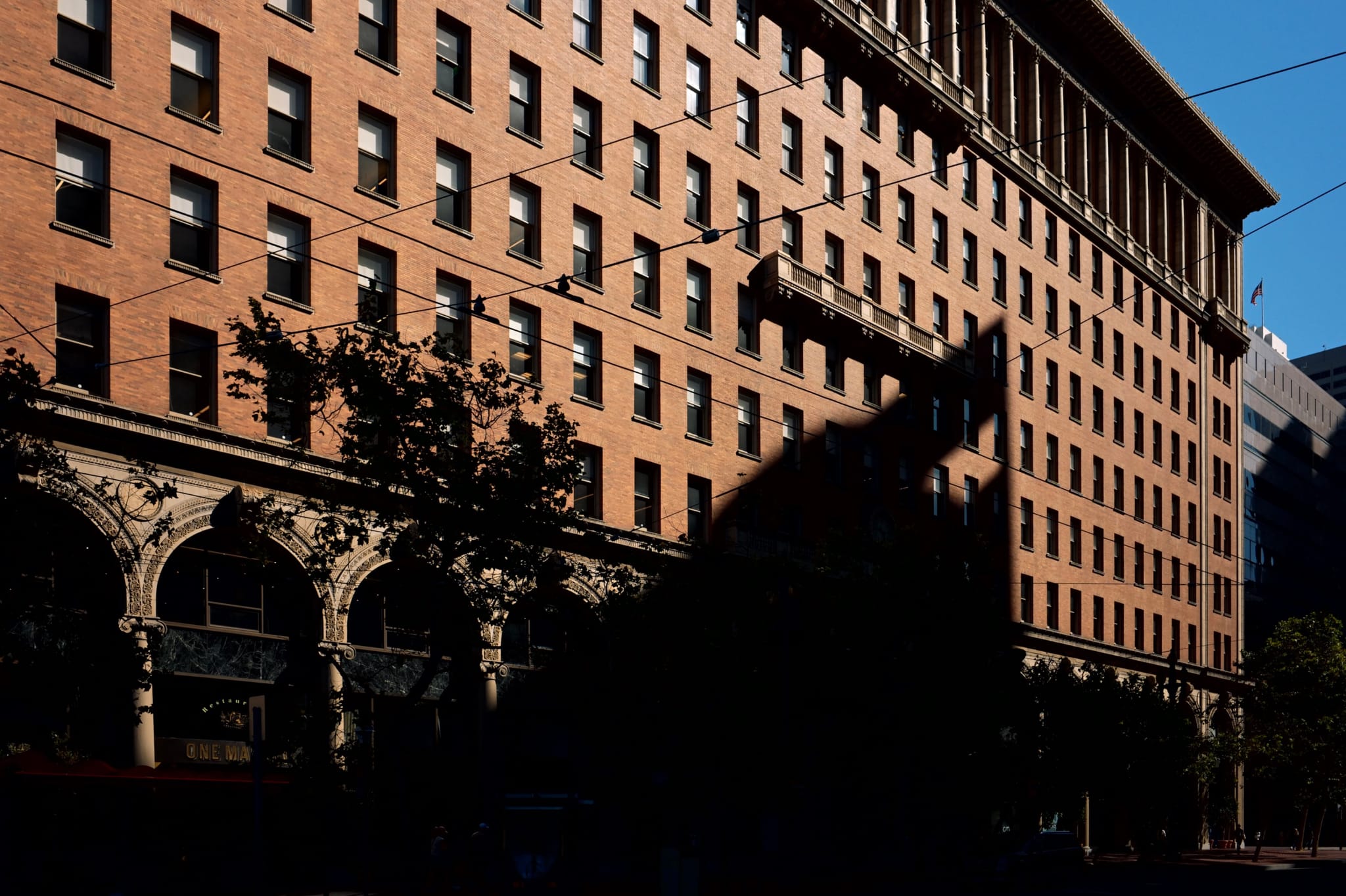 A large brick building with multiple windows, casting a prominent shadow on its facade