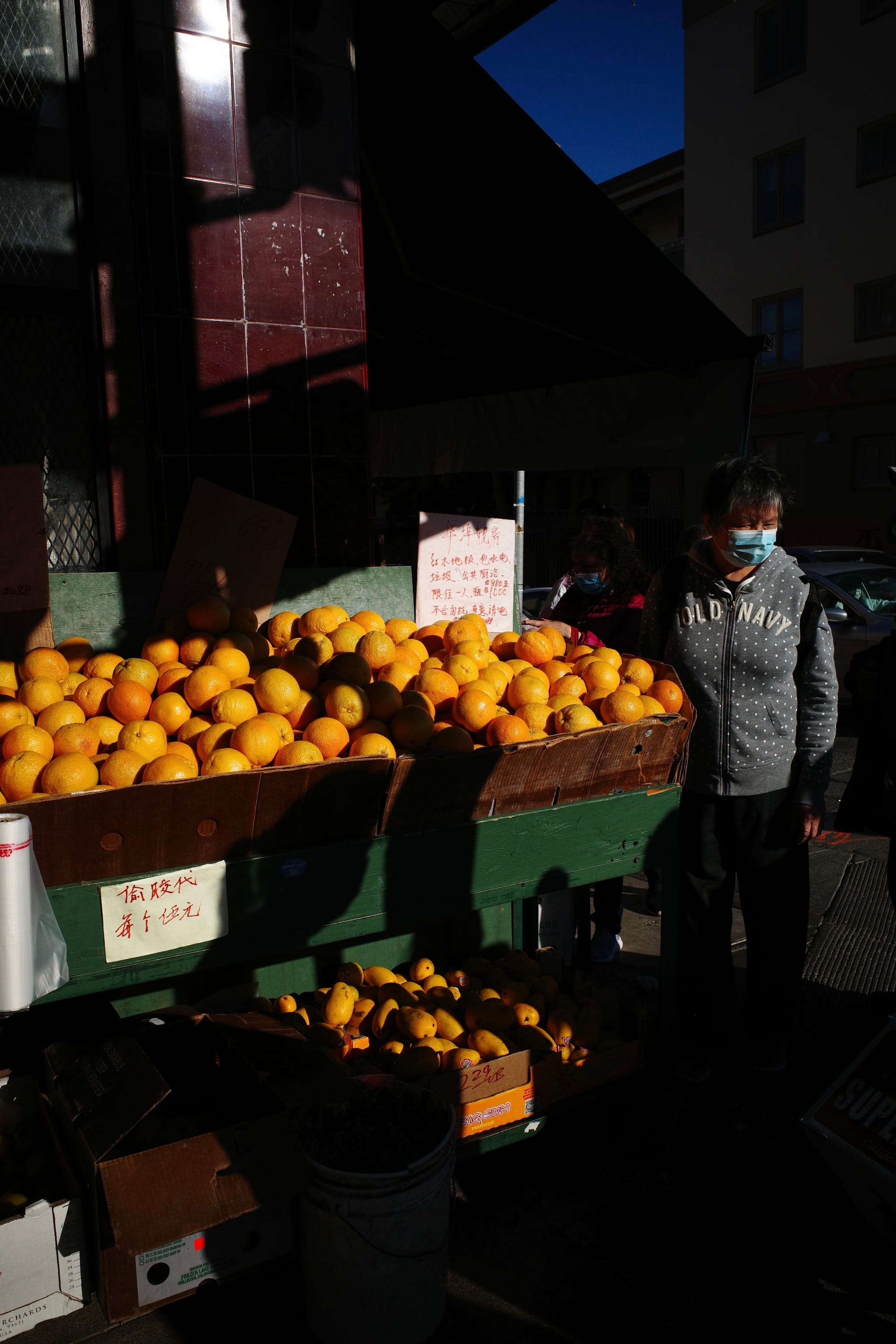 A market stall with a large display of oranges and a person wearing a mask standing nearby