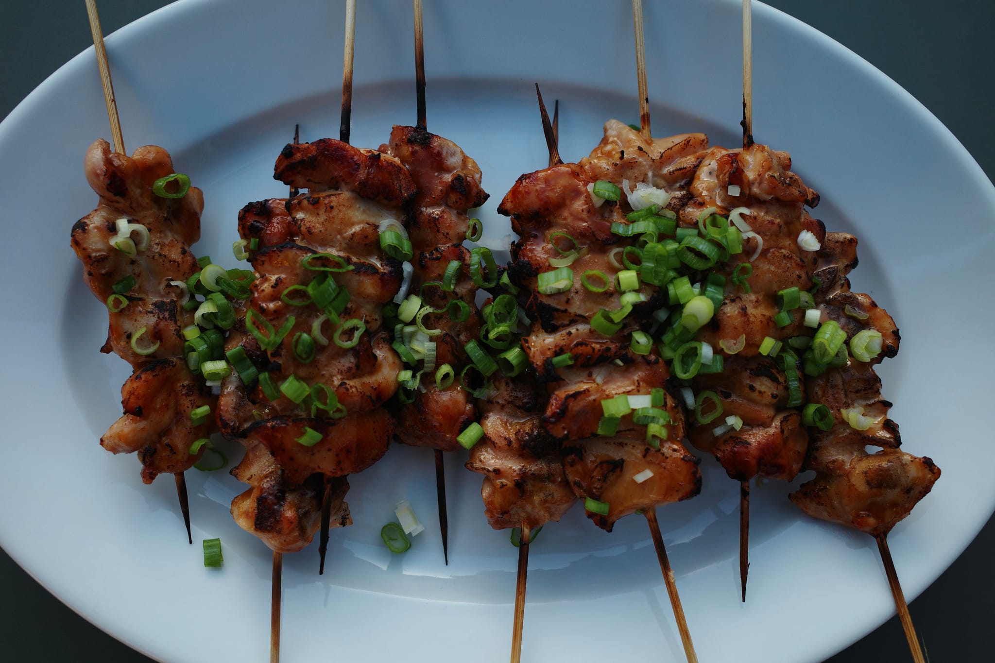 Grilled skewers of meat garnished with chopped green onions on a white plate