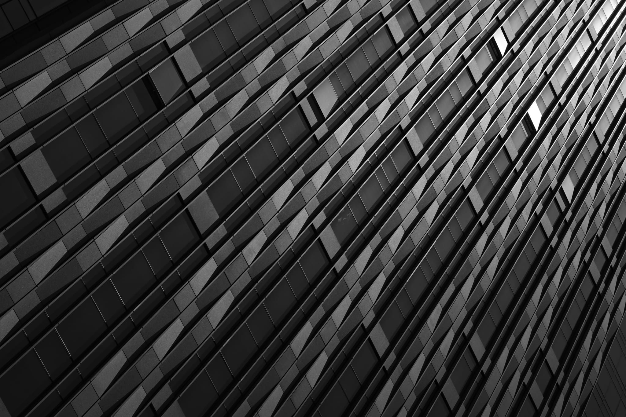 A black and white abstract view of a building facade with a pattern of windows and panels, captured at an angle